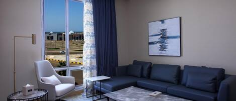 A modern living room with a sofa, armchair, coffee table, and a large window with a view of buildings.