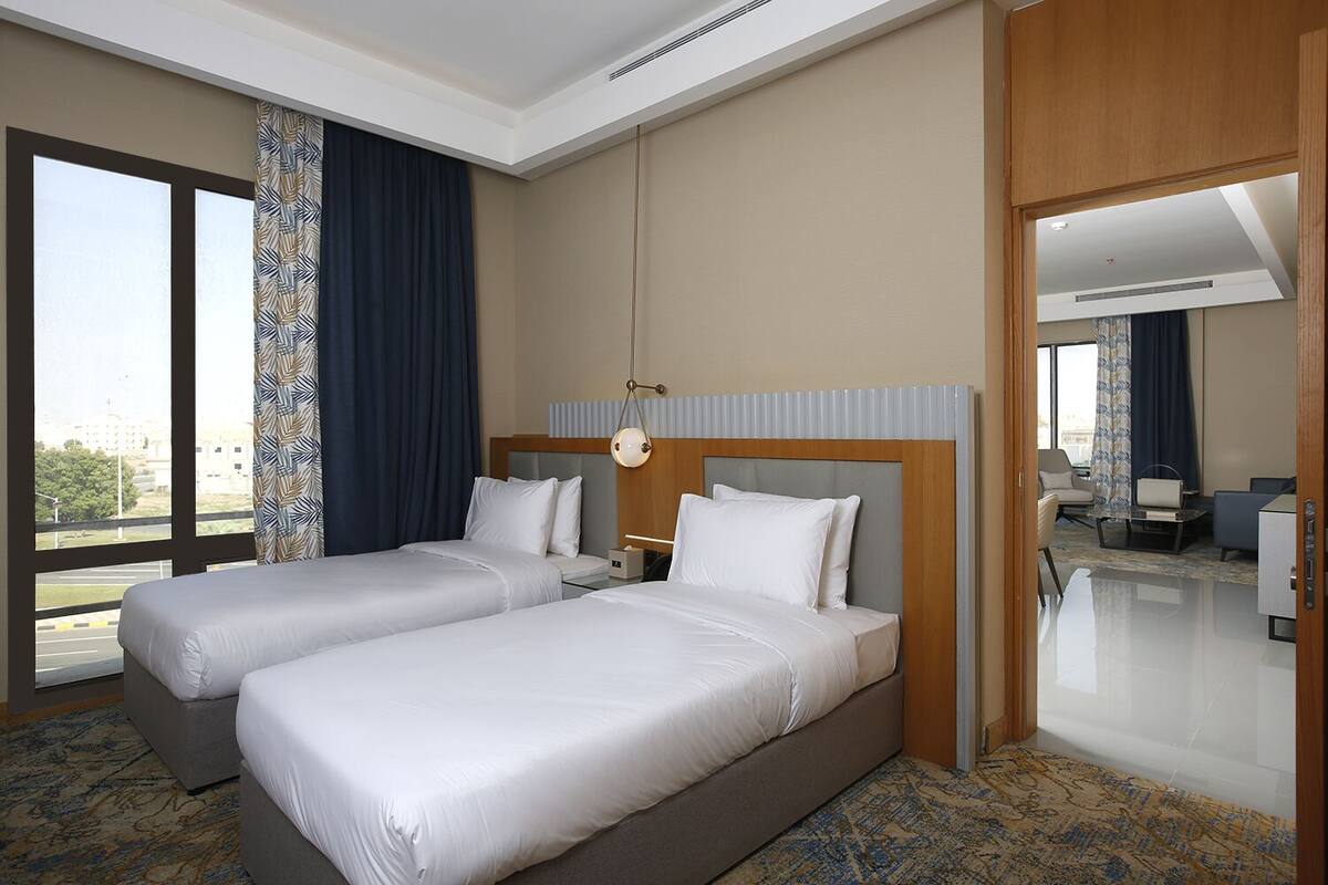 A hotel room with two beds, a large window, a desk, and a chair.