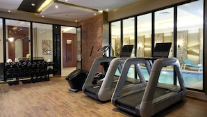 Un gimnasio con cintas de correr, una computadora portátil y vista a la piscina.