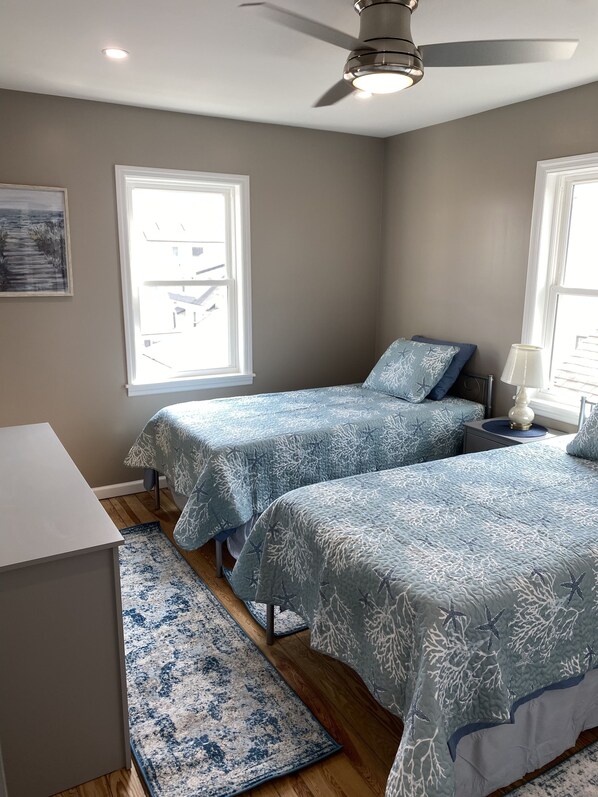 A bedroom with two beds, a ceiling fan, and a window with a view of a building. - Brand New Luxury (Long Beach)