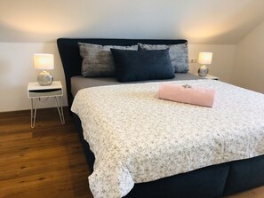 Un lit bien fait, recouvert d’une couvre-lit à motifs floraux, avec deux lampes de chevet et une petite table de chevet sur laquelle se trouve une lampe.