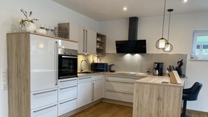 A modern kitchen with white cabinetry, a wooden island, and a black range hood.