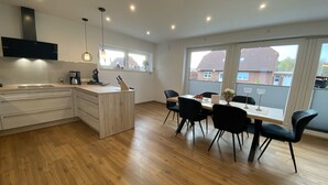 A modern kitchen with wooden cabinets, a central island, and a dining area with black chairs and a wooden table.
