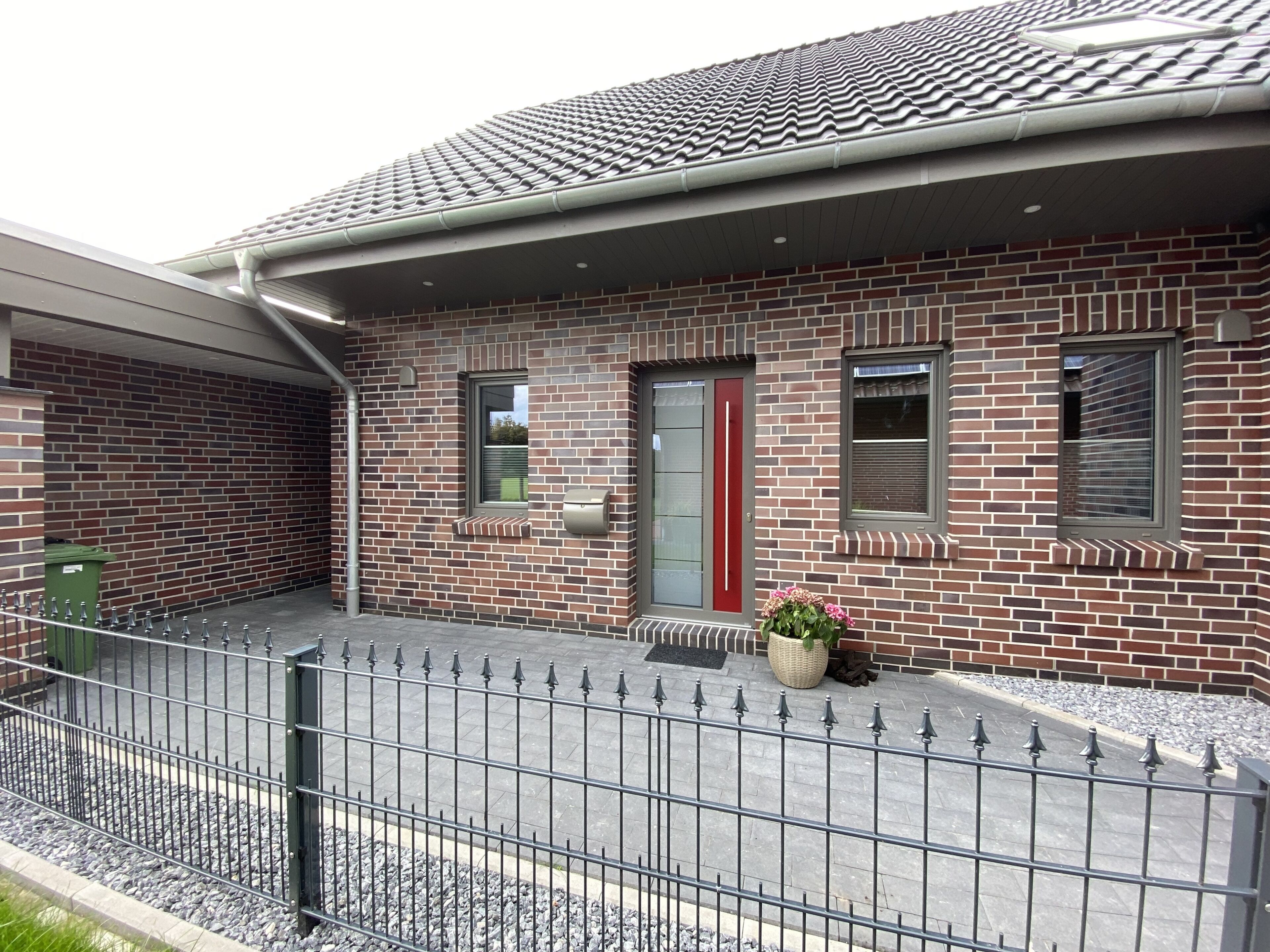 Een gebouw van baksteen met twee verdiepingen, een rode deur, een klein raam en een brievenbus.