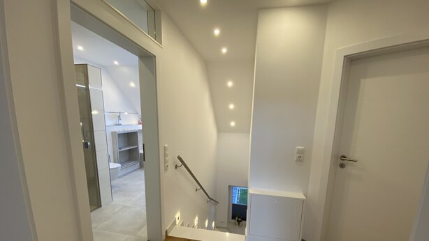 A modern interior with a wooden floor, a white door, and a staircase leading to a second floor.