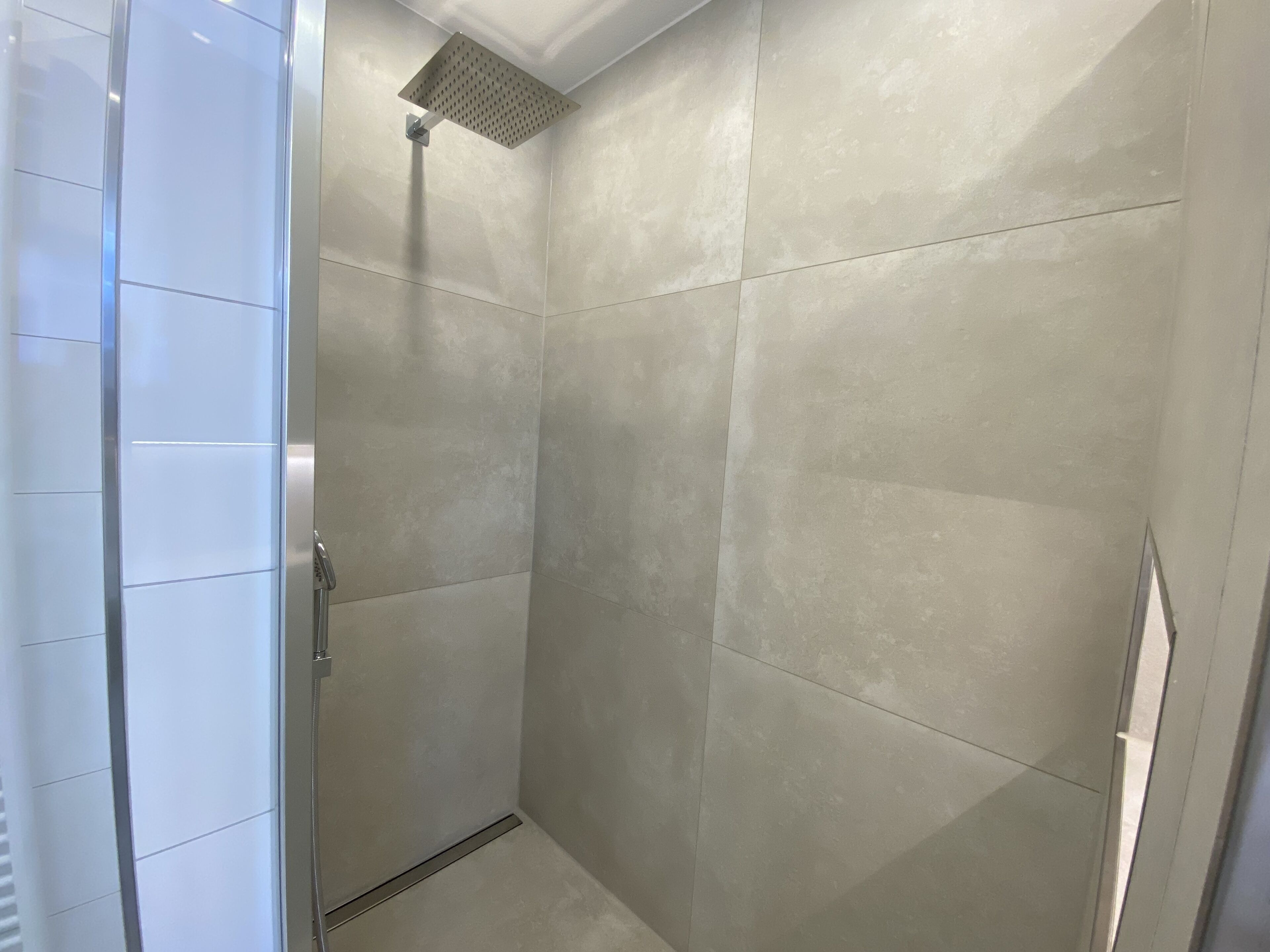 Une douche moderne dotée d’un pommeau de douche carré et d’une porte en verre.