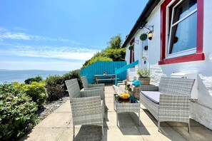 A patio with wicker furniture, a table with fruit, and a view of the sea. - Arthur's Seat,  elevated cottage, sea views (Dunoon)