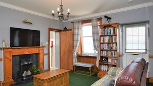 A living room with a fireplace, a television, a bookshelf, and a leather couch. - Arthur's Seat,  elevated cottage, sea views (Dunoon)