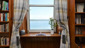 A room with a large window, bookshelves, a small table with a plant, and a desk with a lamp. - Arthur's Seat,  elevated cottage, sea views (Dunoon)