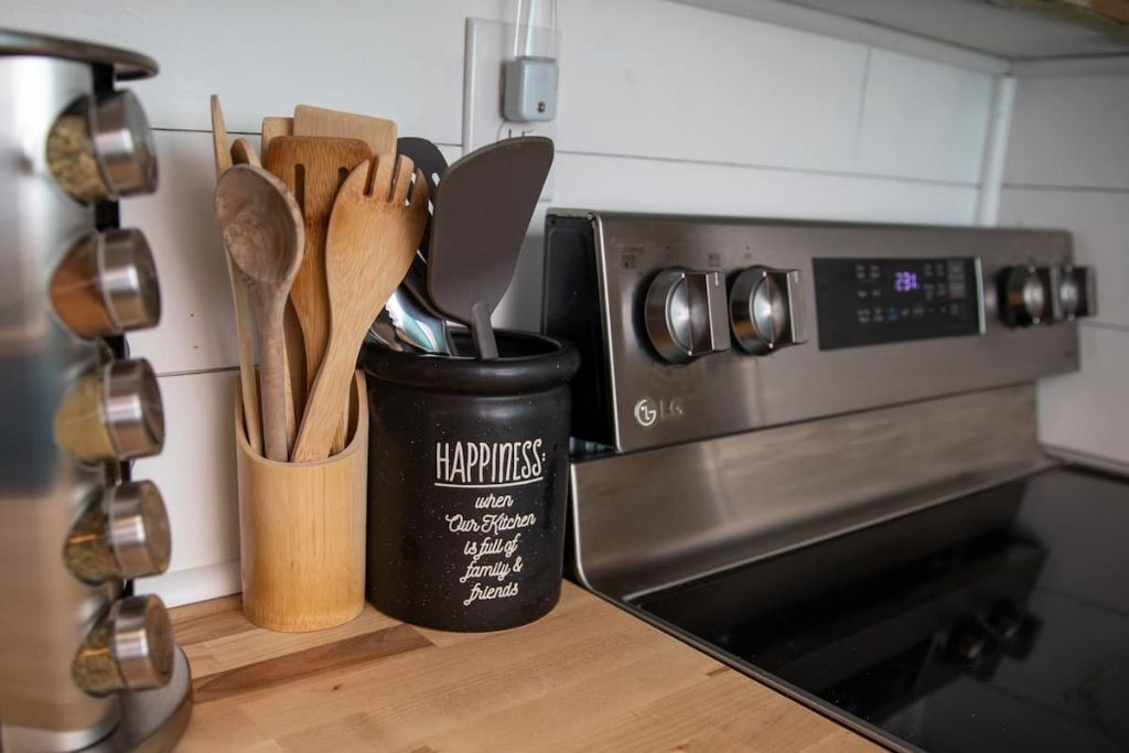 A kitchen with a stainless steel oven, wooden utensils in a holder, and a black container with the word "HAPPINESS" on it.