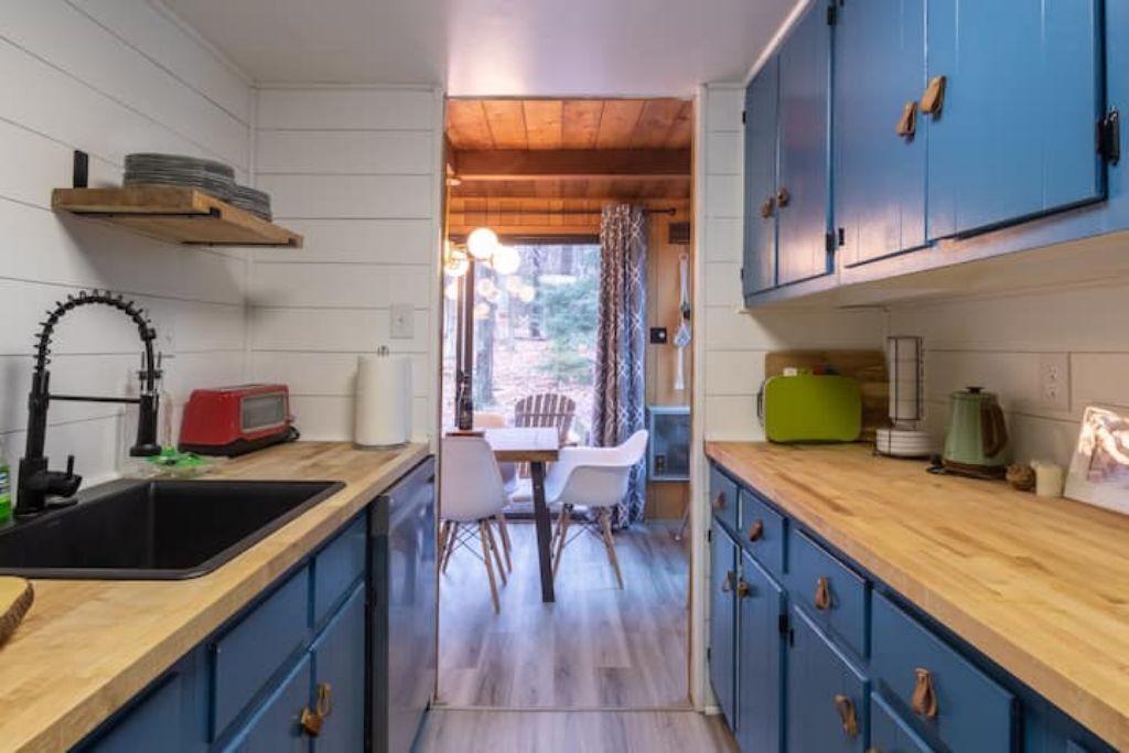 A compact kitchen with wooden countertops, blue cabinets, a sink, and a dining area with chairs and a table.