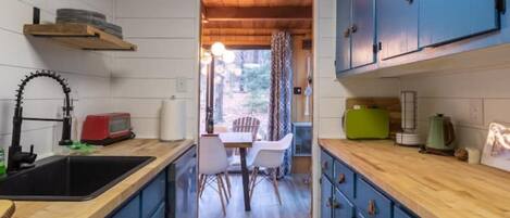 Cocina compacta con encimeras de madera, armarios azules, un lavamanos y un comedor con sillas y una mesa.