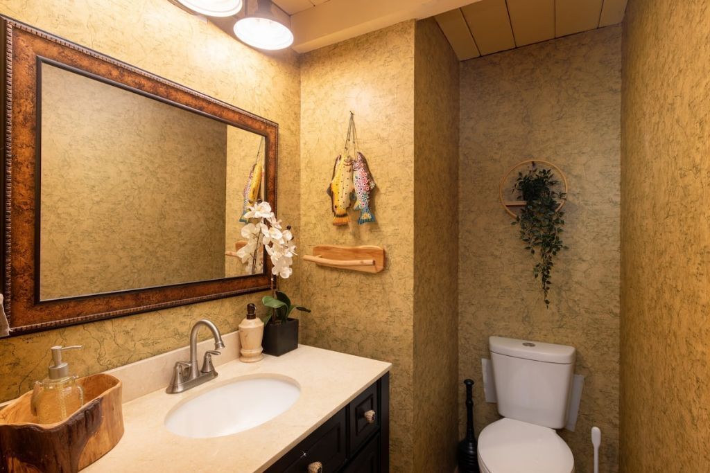 A bathroom with a large mirror, a sink with a wooden basin, a toilet, and a small plant on the wall.