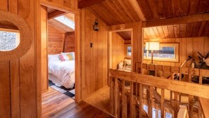 A wooden cabin interior with a bed, a window, and a wooden railing. - Lake Naomi A-Frame Cabin, Pet Friendly, (Pocono Pines)