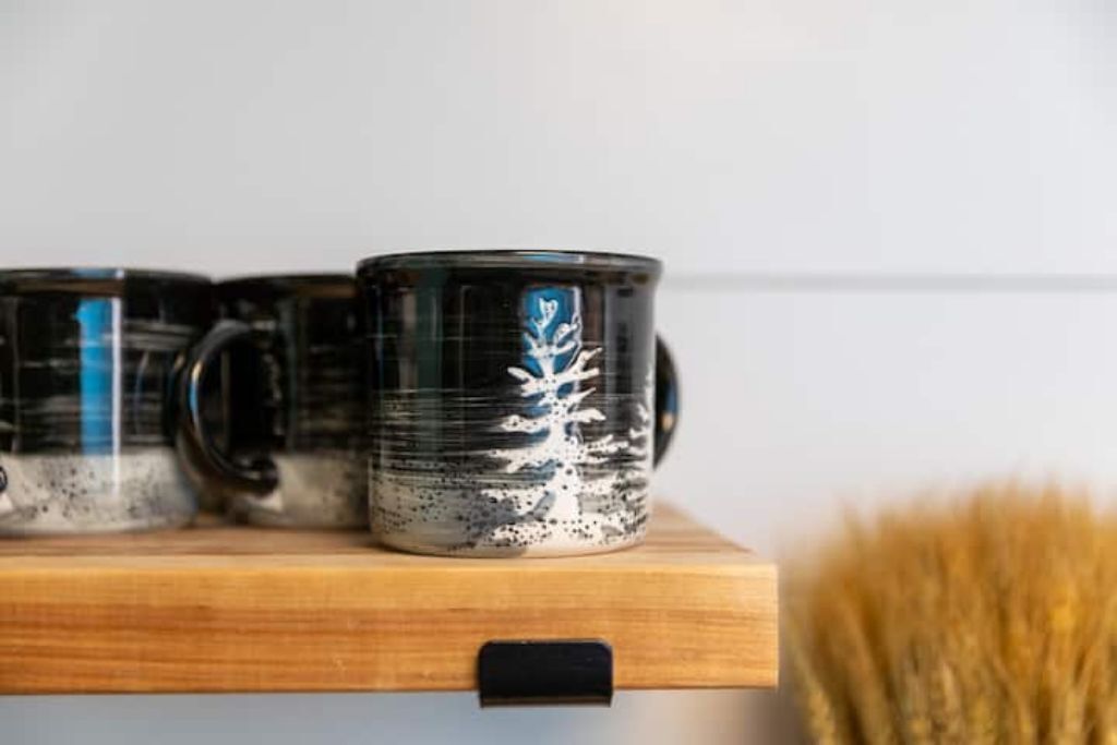 Three black mugs with white designs on a wooden shelf.