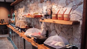 Montaje de bufé con diversos alimentos, una máquina de café y un fondo de pared de piedra.