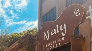 Un hotel boutique llamado 'Maly' con un exterior rústico, que incluye un enrejado de madera y una pared de piedra.