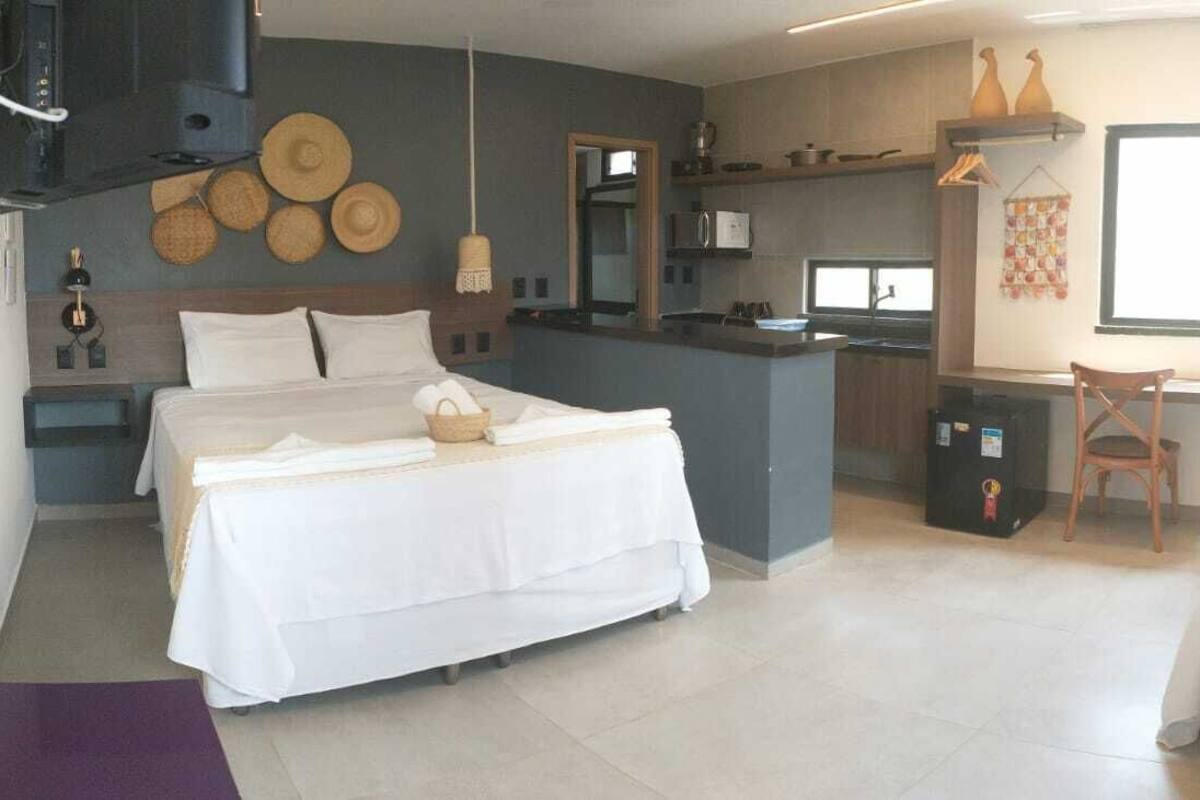 Een moderne hotelkamer met een bed, een bureau, een stoel, een kitchenette en een groot raam.
