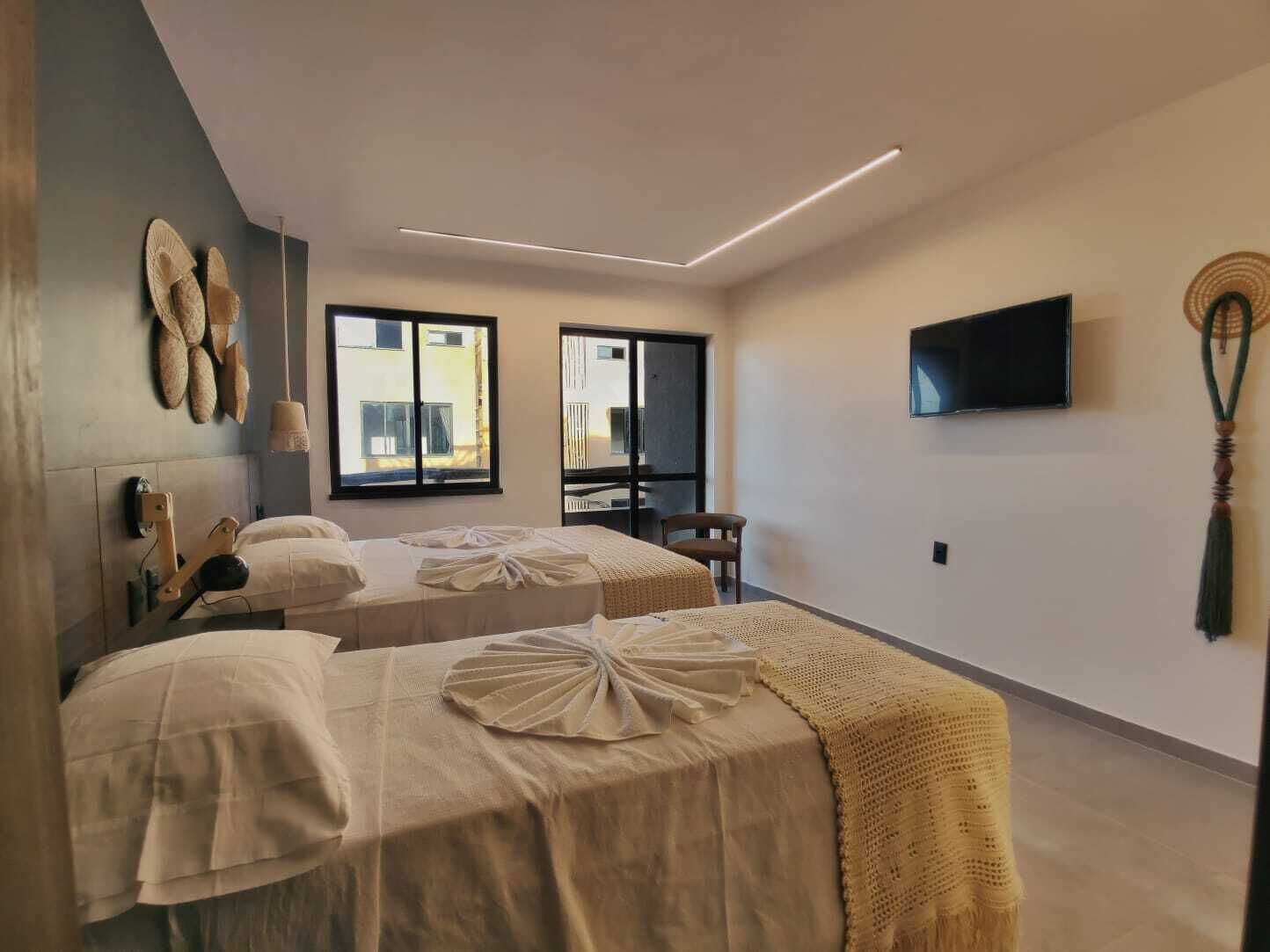 Quarto moderno com duas camas, uma TV de tela plana e uma janela grande.