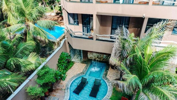 Una piscina con dos sillas de descanso, rodeada de palmeras y un edificio con grandes ventanales.