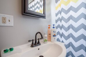 Une salle de bain avec un lavabo blanc, un miroir et un rideau de douche à motifs en zigzag.