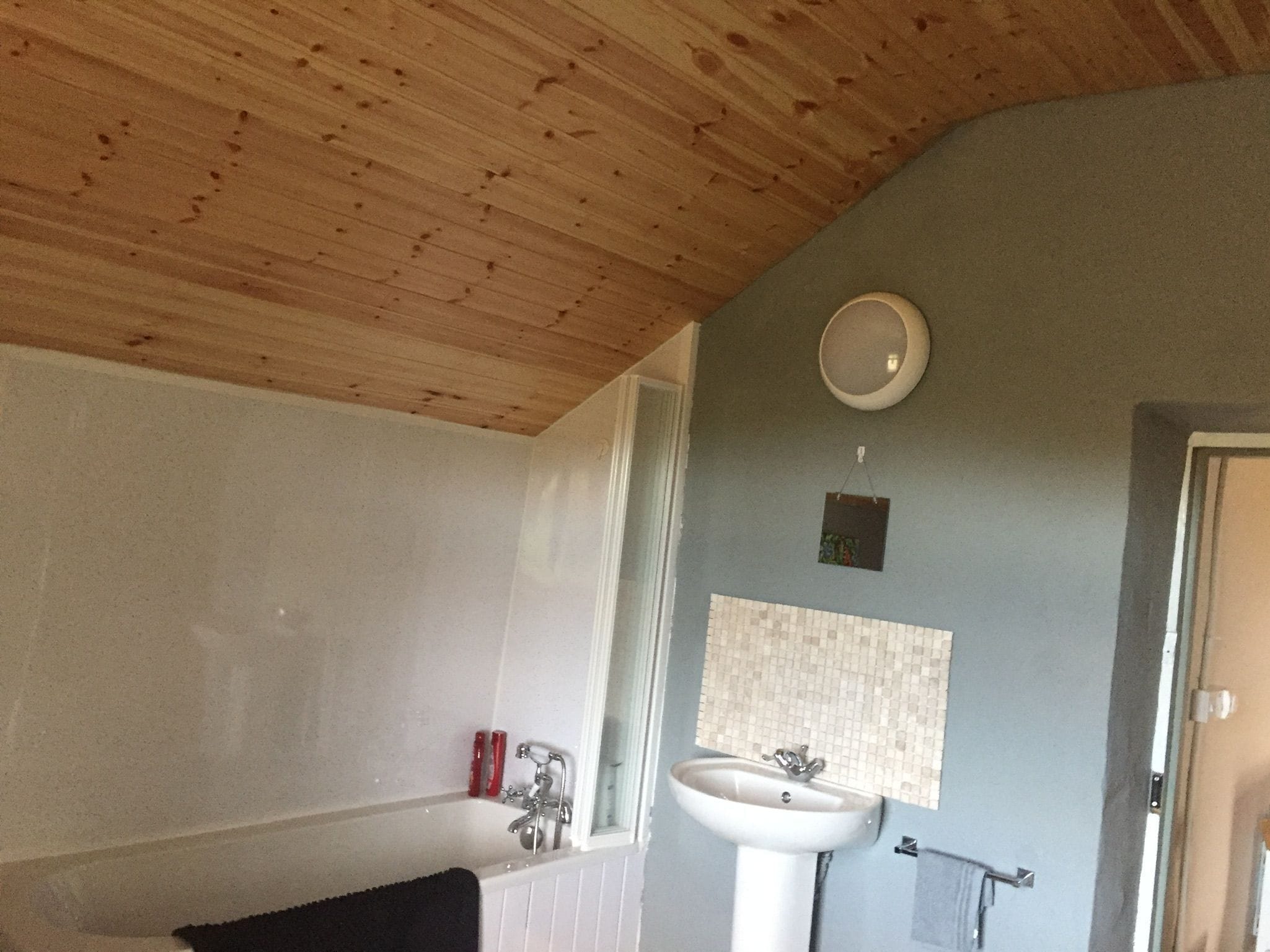 Un baño con techo de madera, una bañera, un lavabo y un espejo.