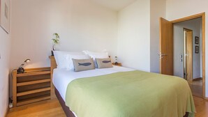 A bedroom with a bed, bedside tables, a lamp, and a door leading to another room. - Design Guincho Villa (Cascais)