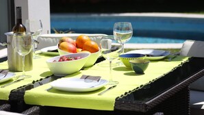 A table set with a bottle, glasses, bowls, and fruits by a poolside. - Design Guincho Villa (Cascais)
