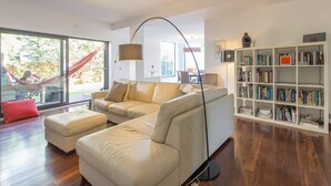 A modern living room with a sectional sofa, a floor lamp, a bookshelf, and a hammock by the window. - Design Guincho Villa (Cascais)