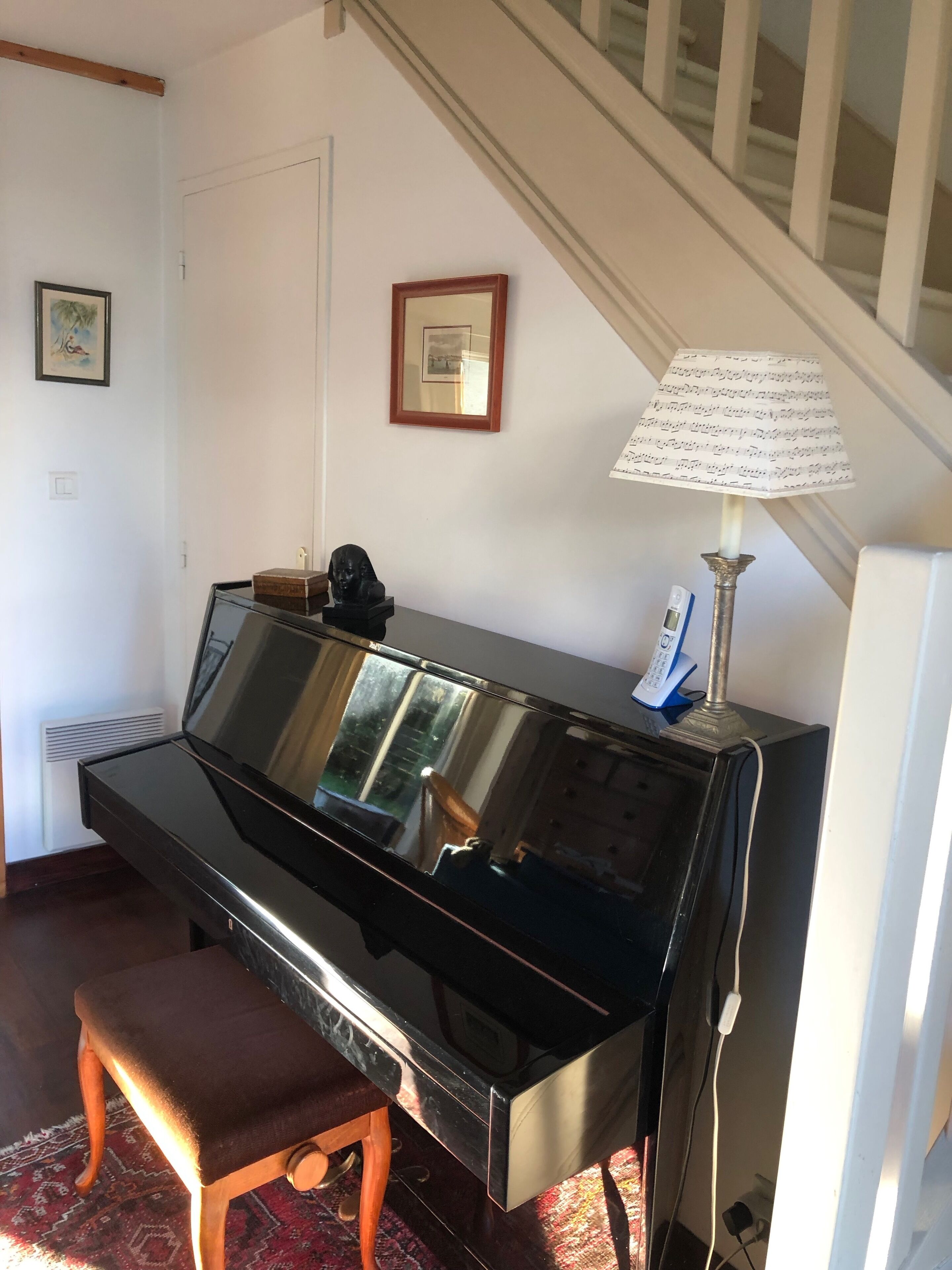 A piano with a bench, a lamp, and a framed picture on the wall.