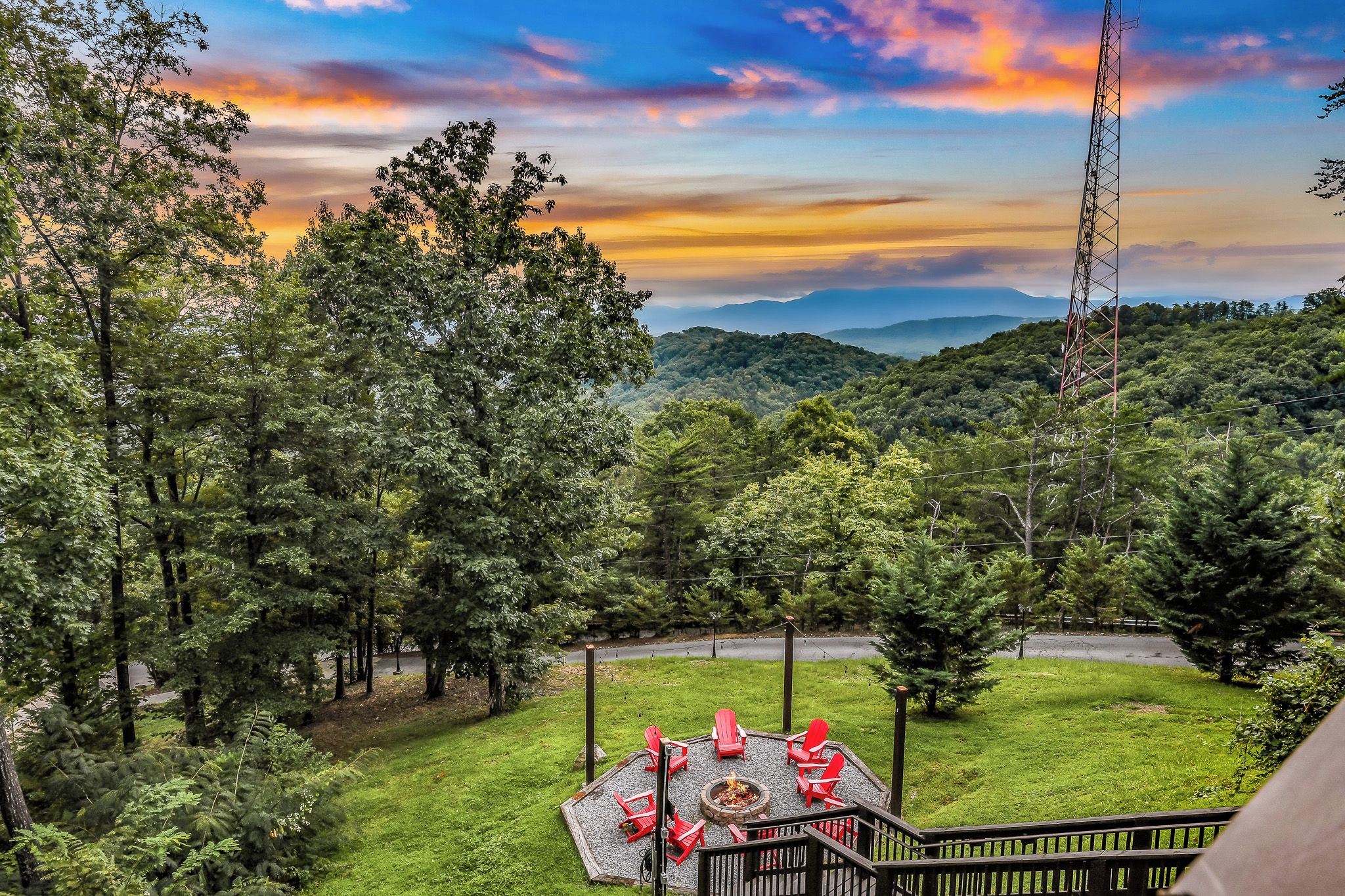 A patio with red chairs and a fire pit, surrounded by lush greenery and a view of distant mountains.