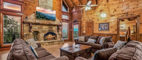 A spacious living room with leather sofas, a stone fireplace, and a large TV screen.