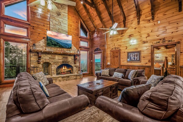 A spacious living room with leather sofas, a stone fireplace, and a large TV screen.