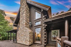A log cabin with a stone chimney, large windows, and a deck.