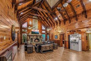A log cabin interior with a fireplace, wooden furniture, and a kitchen area.