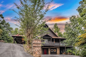 A log cabin with a stone foundation, a balcony, and a red door.
