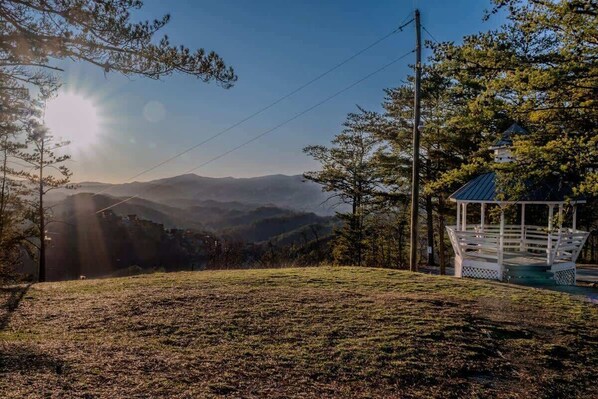 A gazebo in a grassy area with a view of distant mountains and a clear sky.