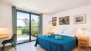 Ein Schlafzimmer mit einem großen Bett, einem Schreibtisch, einem Stuhl und Blick durch eine Schiebetür.