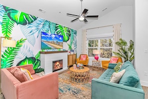 A living room with a fireplace, a ceiling fan, and a large window.