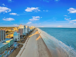 A coastal cityscape with a long beach, high-rise buildings, and a clear sky.