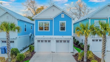A residential area with three houses, each with a garage and a front yard with palm trees.