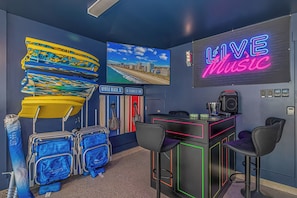A room with a neon 'LIVE MUSIC' sign, a beach view, a seating area with a bar, and luggage storage.