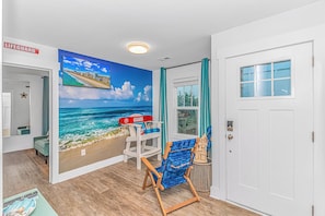 A room with a beach mural, a lifeguard chair, a wooden door, and a small window. - Beach Cottage: Glow Arcade + Aquarium Bunk Room (Myrtle Beach)