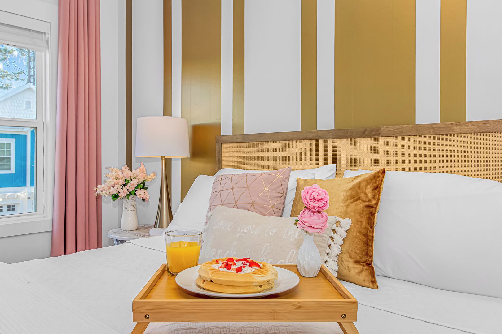 A hotel room with a bed, a bedside table with a lamp, a tray with breakfast, and a window with curtains.