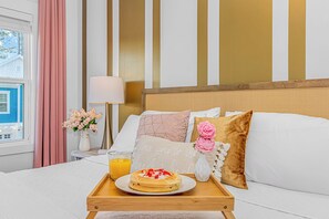 A hotel room with a bed, a bedside table with a lamp, a tray with breakfast, and a window with curtains.