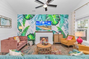 Una sala de estar con chimenea, televisor y papel tapiz tropical.