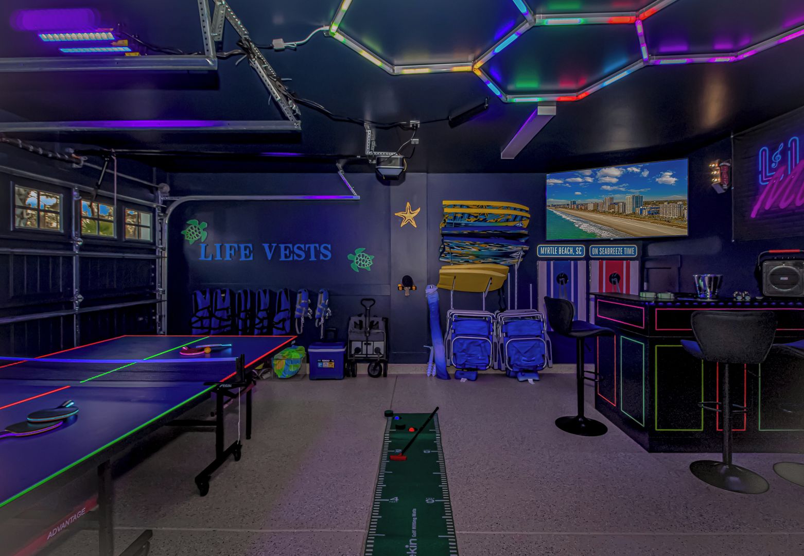 A room with a ping pong table, life vests, a star decoration, a beach scene on the wall, and a desk with a computer.