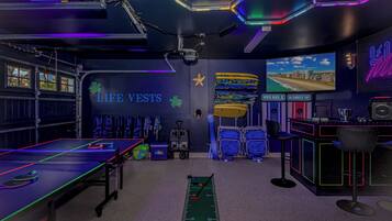 A room with a ping pong table, life vests, a star decoration, a beach scene on the wall, and a desk with a computer.