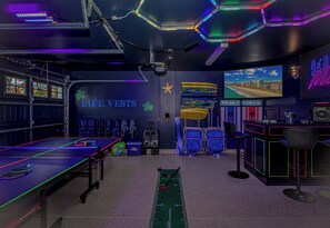 Une pièce avec une table de ping-pong, des gilets de sauvetage, une décoration en forme d’étoile, une fresque représentant une plage sur le mur et un bureau avec un ordinateur.