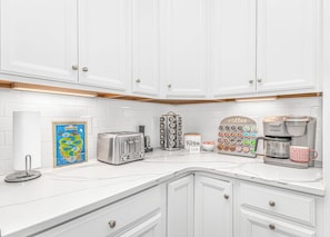 A kitchen with white cabinets, a toaster, a coffee maker, and a coffee mug.
